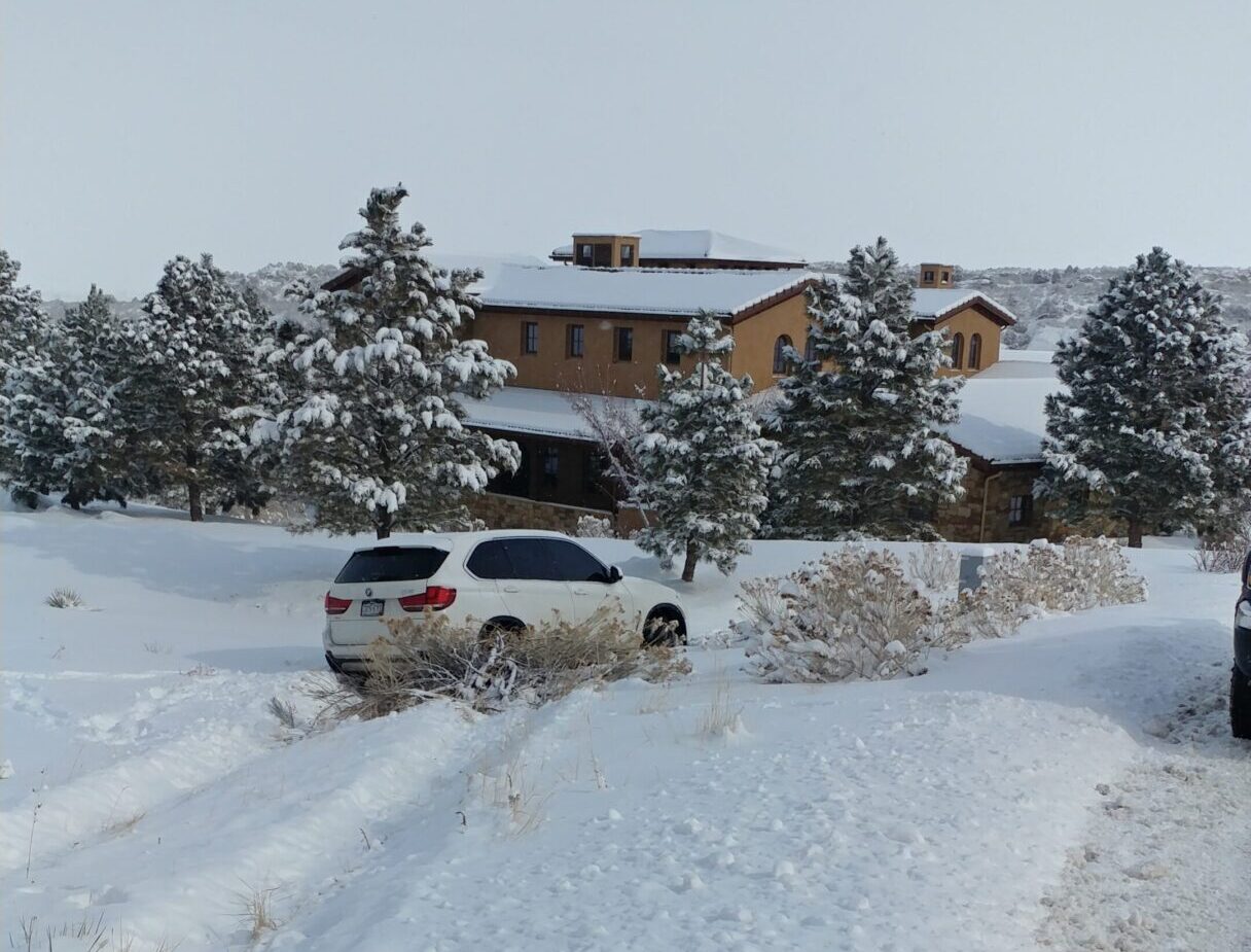 SUV driving through deep snow near a wooden cabin in winter.